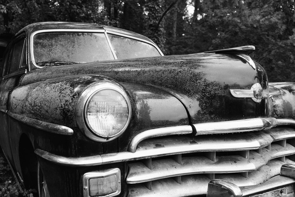 Black and white photograph of a big shiny black antique Chrysler that's beginning to lose its luster in a junkyard in the American South.