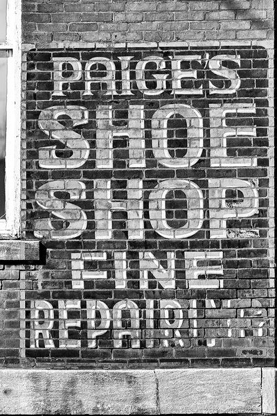 Black and white photograph of a historic painted "ghost ad" for the now defunct Paige's shoe shop seen on a brick wall in Hopkinsville, Kentucky.