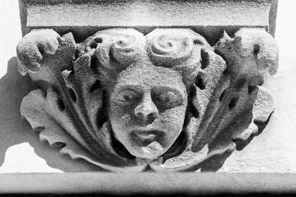 Black and white photograph of female cherub face centered amongst leaves carved in stone on a building constructed in 1902. Originally built for a regional telephone and telegraph company, the building later became a lodge for the International Order of Odd Fellows (I.O.O.F).