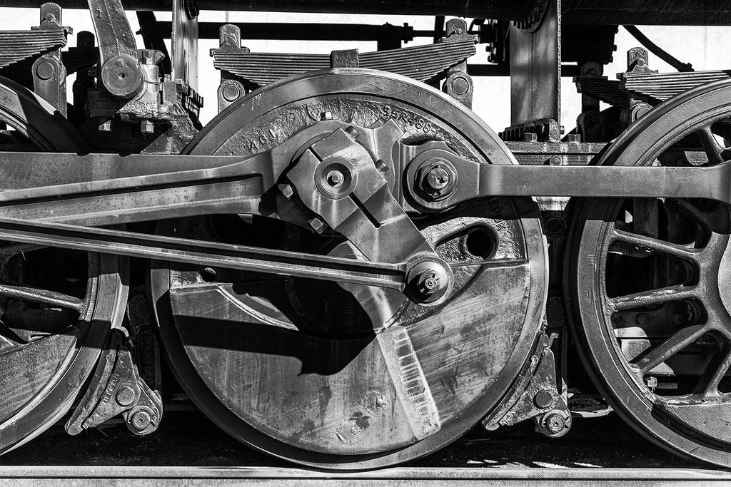 Black and white photograph of the wheels of an old locomotive on the tracks.