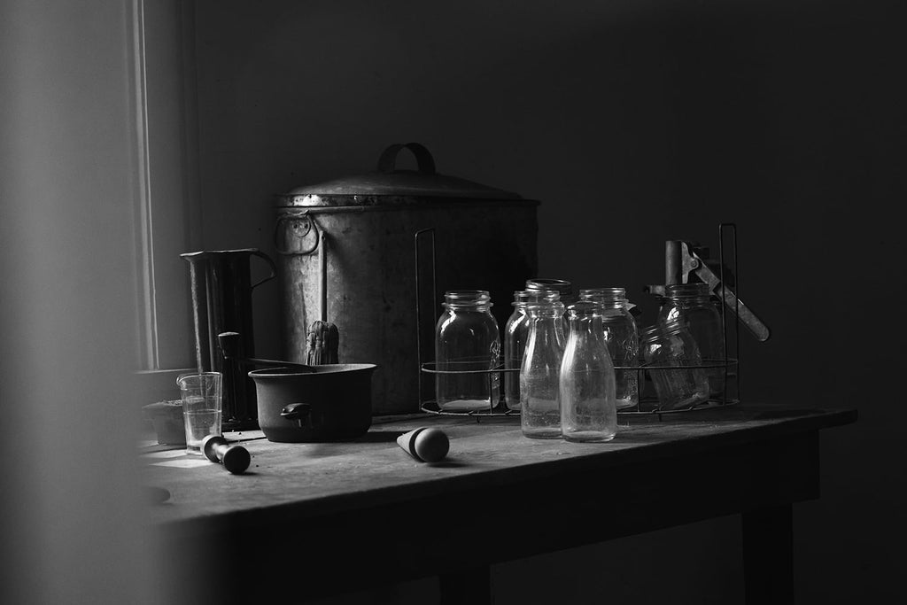 Black and white photograph of Bell jars and pots in the kitchen of a very old house shot in natural light