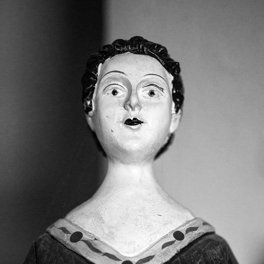 Black and white photograph of an antique wooden doll figurine found in an old house, photographed portrait style. (Square format)