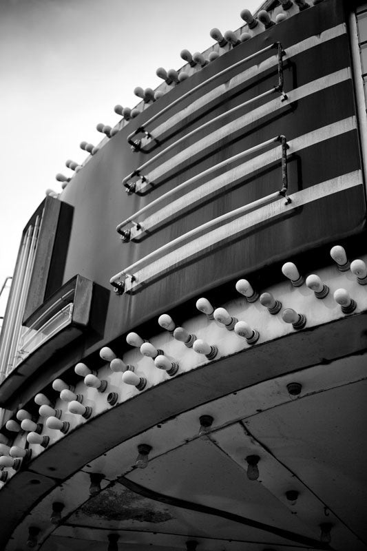 Black and white photograph of a vintage theater marquee in a small town, showing rows of light bulbs and curving neon.