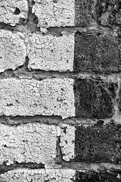 Black and white detail photograph of paint chipping and peeling from old bricks on a small town building.