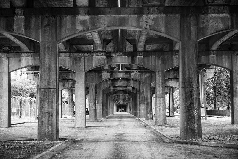 Black and white photograph under the 1st Avenue North bridge that runs near the Sloss Furnaces in an industrial area near downtown Birmingham, Alabama.