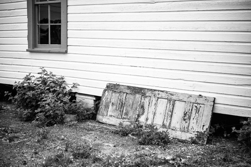 Black and white photograph of an old house with a peeling antique wooden door propped against an outside wall, in Birmingham, Alabama.