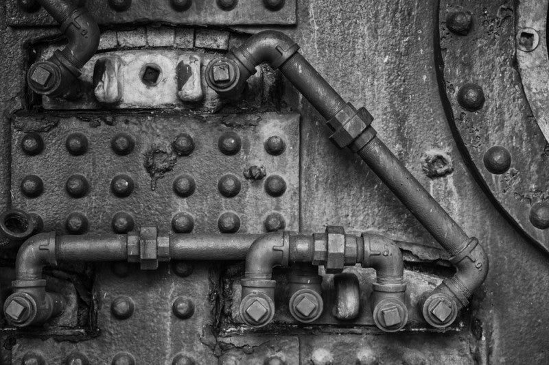Black and white retro industrial photograph of pipes, rivets, and fittings.