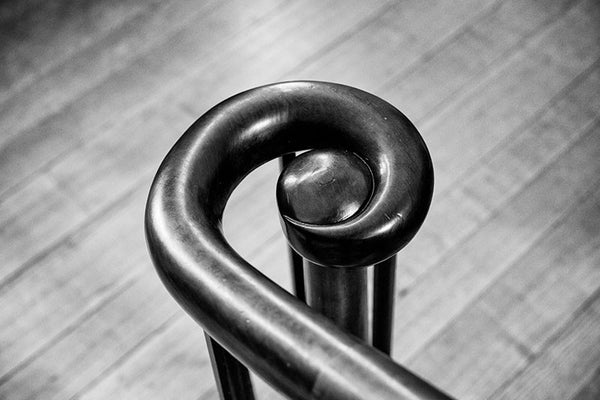 Black and white photograph of an antique handrail that terminates in a spiral, found in an old house that was built in stages between 1810 and 1850. This minimalist image was composed to emphasize the graceful curve of the rail, and the diagonal lines of the wooden floorboards.