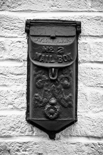 Black and white photograph of old-fashioned metal mailbox on the brick wall of a historic building in St. Charles, Missouri.