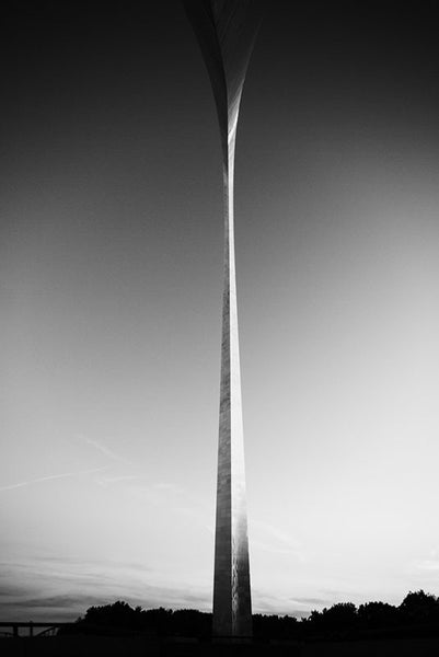 Black and white photograph in a super-wide angle view from directly under the famous St. Louis Gateway Arch at sunset. 