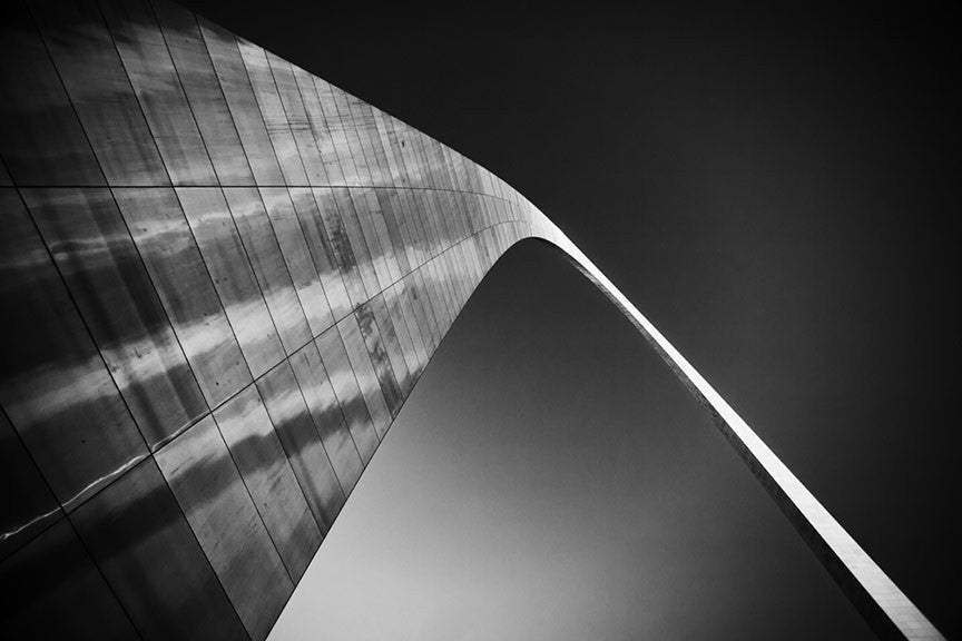 Black and white photograph of the famous St. Louis Gateway Arch against a dark sky, catching the last rays of light at sunset. 