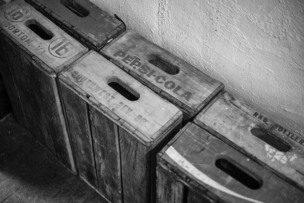 Black and white detail photo of vintage wooden soft drink crates stacked against the wall in an old house.
