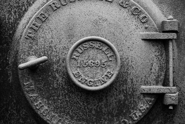 Black and white photograph of a rusty antique machine door marked by the Russell Engine Company.