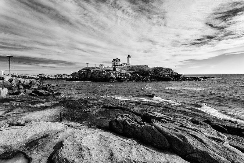 Black and white photograph of the beautiful Nubble lighthouse, which sits on a tiny island just yards off the coast at York, Maine. The lighthouse, officially called the Cape Neddick Lighthouse, began service in 1879 and is still in operation today. The lighthouse sits 88 feet above sea level atop the rocky Nubble islet.