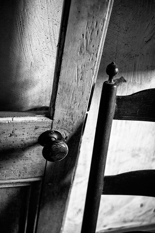 Black and white photograph of an old French-style door and wooden chair inside an old house in Lafayette, Louisiana.
