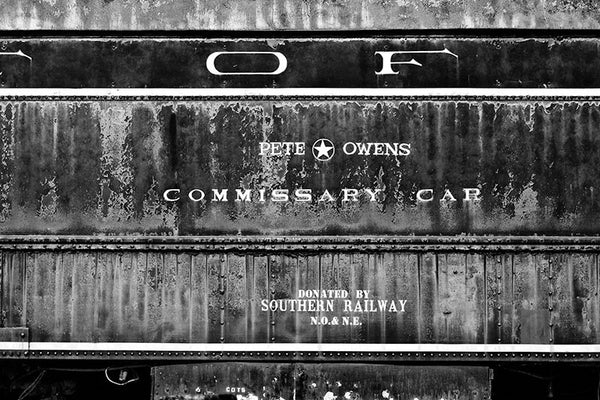 Black and white photograph of an abandoned, rusty and peeling Pete Owens Commissary train car.