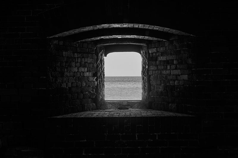 Black and white architectural photograph of the Gulf of Mexico, as seen through one of the heavy brick gun ports at Civil War-era Fort Massachusetts, on Ship Island, Mississippi.