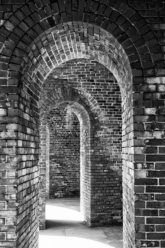 Black and white photograph of a corridor of repeated arched brick doorways, captured in dramatic lighting.