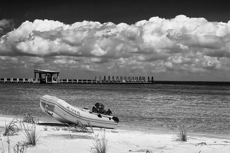 Black and white photograph of a boat pulled ashore on an island in the Gulf of Mexico off the coast of Mississippi, with a huge bank of clouds on the horizon.