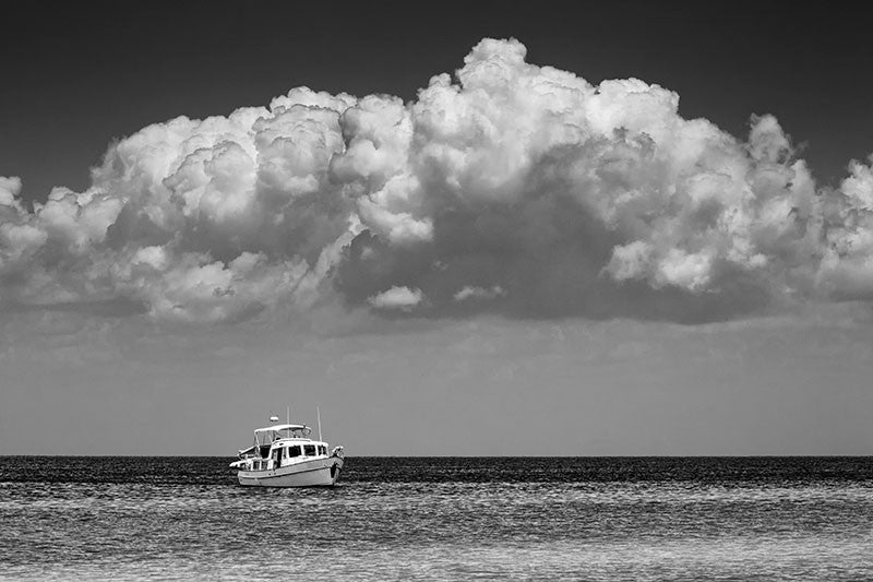 Black and white photograph of a boat anchored near an island in the Gulf of Mexico off the coast of Mississippi, with a huge bank of clouds over head.