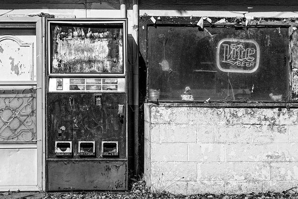 Black and white photograph of an abandoned bar and vending machine found along a country highway.