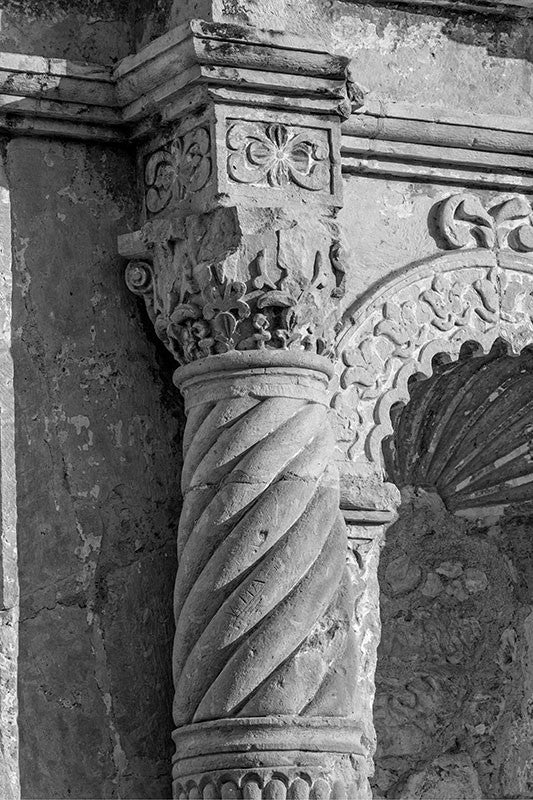 Black and white detail photograph of one of the carved stone columns on the front of the world-famous Alamo, cradle of Texas independence from Mexico in San Antonio, Texas. This architectural detail photograph illustrates the ornate stone carvings and textures of the building, which began existence as a Spanish mission in 1744, known originally as Misión San Antonio de Valero.