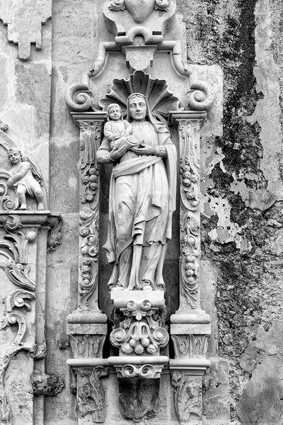 Black and white fine art photograph of the carved stone sculpture of St. Anne with Mary on the limestone exterior on the old Spanish Mission San Jose in San Antonio.