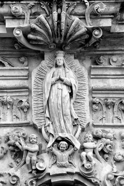 Black and white fine art photograph of the ornate statue of Our Lady of Guadalupe carved into the limestone facade on the old Spanish Mission San Jose in San Antonio.