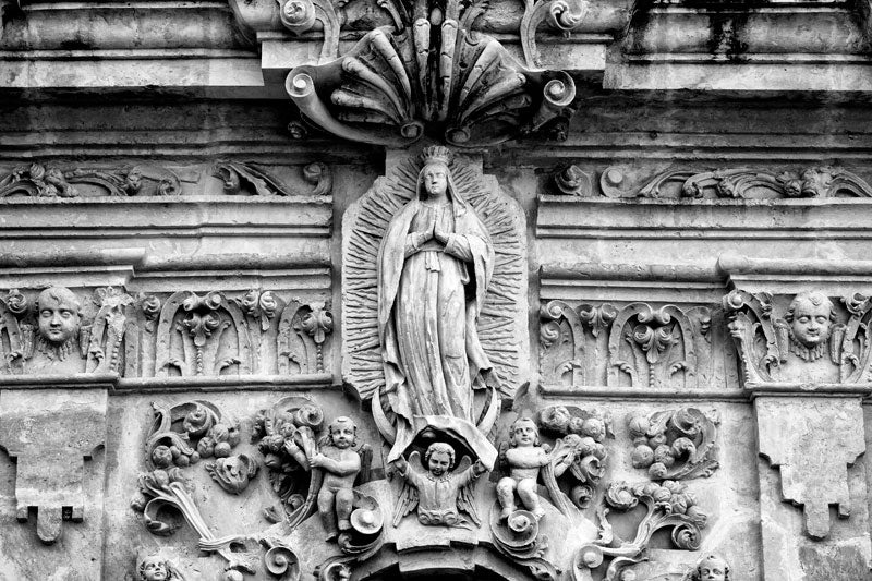 Black and white fine art photograph of the ornate carved stone relief sculpture on the exterior on the old Spanish Mission San José in San Antonio, Texas.