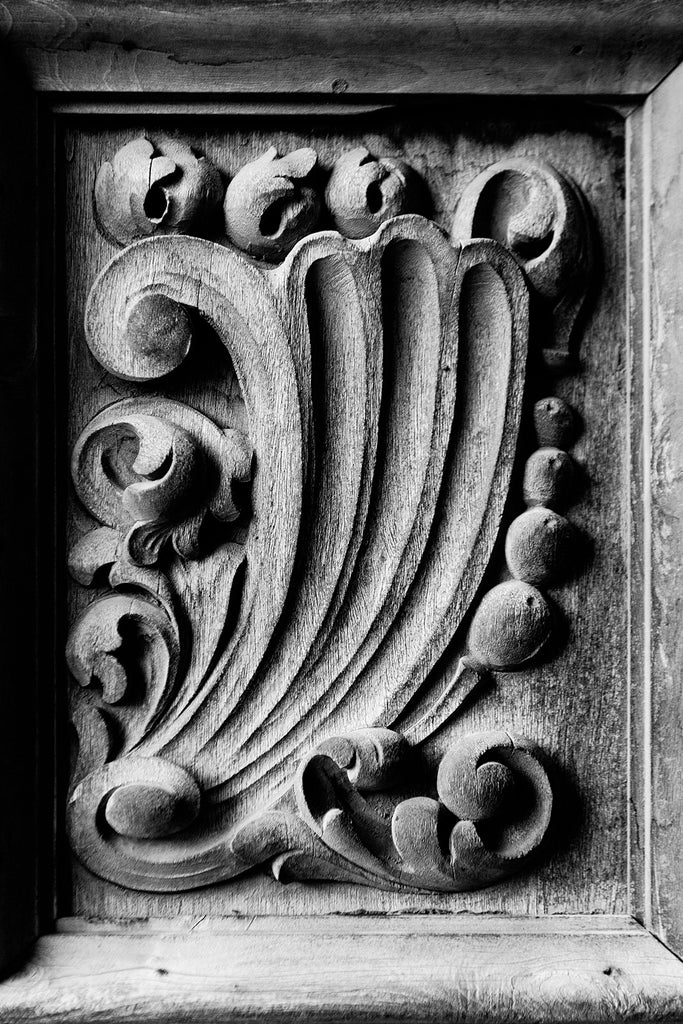 Black and white photograph of one of the rustic hand-carved wooden chapel doors at Mission San Jose in San Antonio, Texas. The wave motif may symbolize the ocean voyage that delivered the missionaries from Spain to the new world.