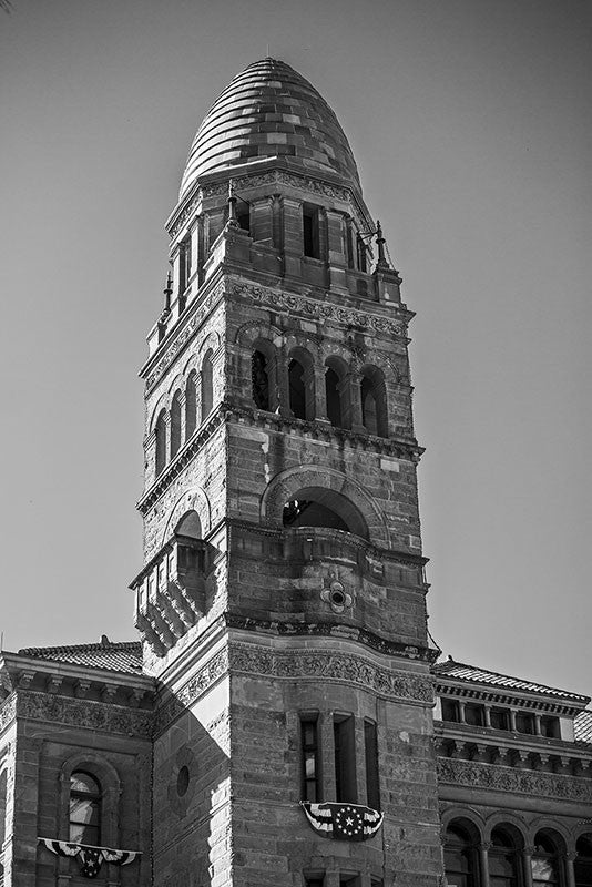 Black and white photograph of the tower of Bexar County Courthouse, a red sandstone building opened in 1896. Designed in the Romanesque revival style by architect James Riley Gordon, the courthouse sits in San Antonio's Main Square, adjacent to the historic Cathedral of San Fernando. 