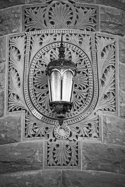 Black and white photograph of a lamp on the ornately patterned stone of the old Bexar County Courthouse in San Antonio.