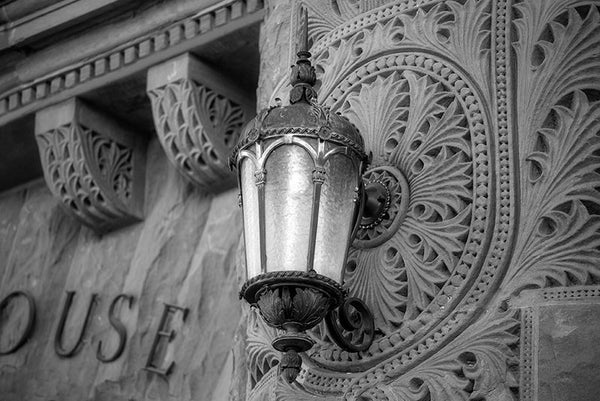 Black and white photograph of a lamp on the ornately patterned red sandstone exterior of the old Bexar County Courthouse in San Antonio, in service since 1896.