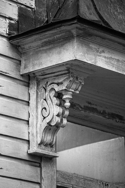 Black and white architectural detail photograph of antique wooden corbel under the eave of a porch an old house in Charleston, South Carolina.
