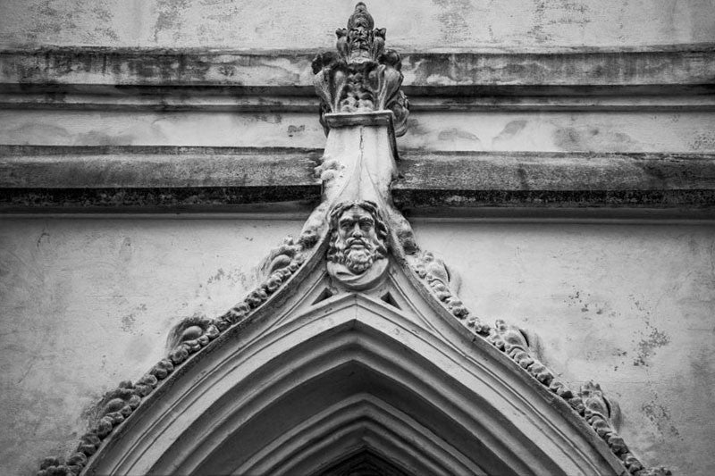 Black and white architectural detail photograph of a face carved atop the apex of a pointed arch in Charleston, South Carolina. 