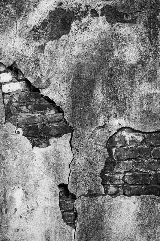 Black and white architectural detail photograph of a bricks peeking through the cracked cement of an exterior wall at the old Charleston Jail, which was served from 1802 until 1939.