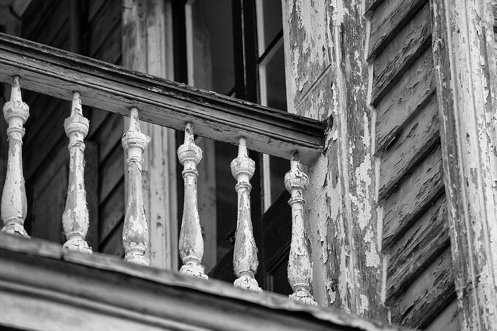 Black and white architectural detail photograph of antique wooden handrail on the second story porch an old house in Charleston, South Carolina.