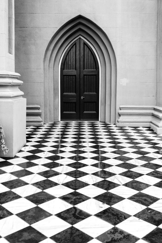 Black and white photograph of a historic churchyard in Charleston that features striking fence-to-fence checkerboard tiles. 