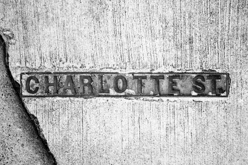 Black and white photograph of a Charlotte Street sidewalk sign in historic Charleston, South Carolina.