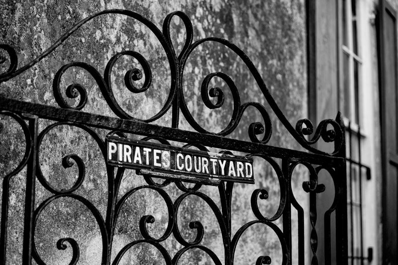 Black and white photograph of an ornamental iron work gate for the Pirate's Courtyard in the French Quarter area of Charleston, South Carolina. 