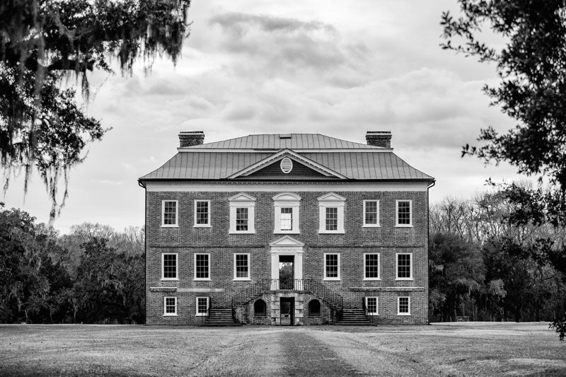 Black and white photograph of the front exterior of Drayton Hall, nine miles outside Charleston. Drayton Hall was built about 1740, and is the only South Carolina plantation home to survive the Revolutionary War and the Civil War intact. The house is now held in a state of preservation, maintained but not restored, which means that original paint, woodwork, and carved ceilings can still be seen.