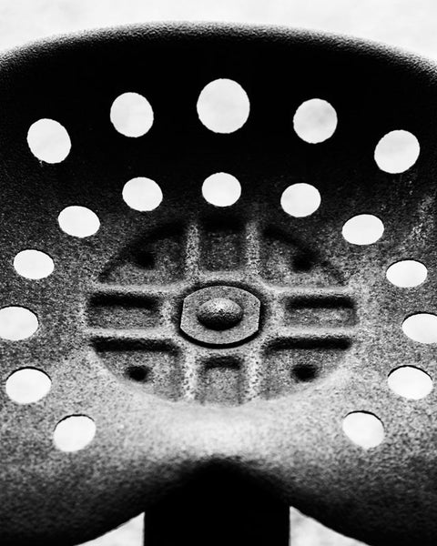 Black and white detail photograph of a rusty tractor seat on an antique tractor, cropped close to reveal details, textures, and the rivet in the center.