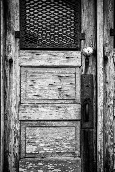 Black and white photograph of an rustic, weathered wooden door on the old drugstore in St. Augustine, Florida. The old Speissegger Drugstore in St. Augustine's old town was built as part of an upscale Victorian development in 1886 and operated as a drugstore / pharmacy until the 1960s. It's the last remaining structure from that development.