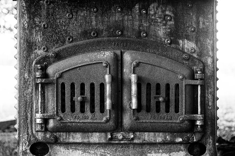 Black and white photograph of the grimy iron doors of an antique furnace.