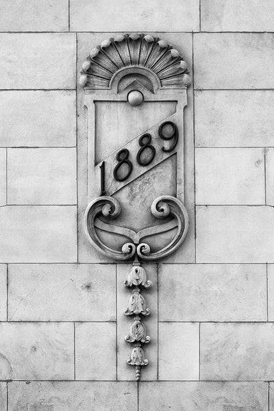 Black and white photograph of an architectural detail featuring the date "1889" embellished across a crest, on the old Nashville Trust Building (now the Hotel Indigo). The crest features a scalloped clam shell motif of waves above the top edge, and flowers in a row along the bottom.