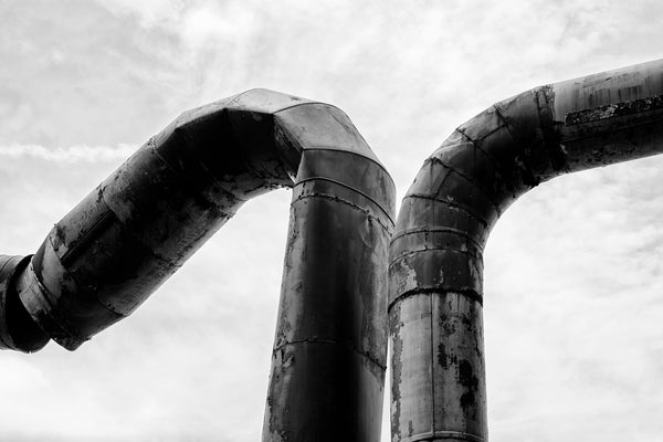 Black and white industrial photograph of two rusty pipes on a derelict piece of industrial machinery.