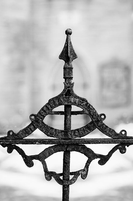 Black and white photograph of a beautifully ornate but rusty detail on the antique iron gate at Holy Trinity Church, built circa 1852, near downtown Nashville, Tennessee. The church was designed by architects Frank Wills and Henry C. Dudley. The old gate detail is difficult to read, but it's a logo for the iron works that made the gate and fence, and says "[Unknown] Architectural Iron Works."