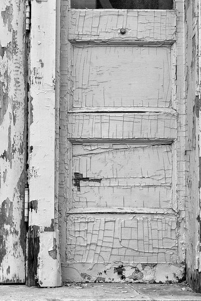 Black and white photograph of cracked and peeling paint on the door of an abandoned building.