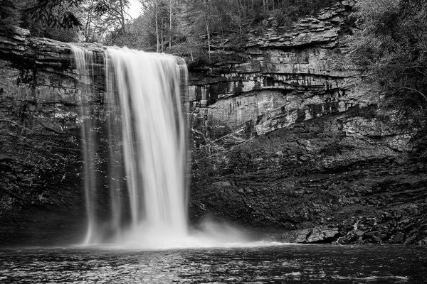 Black and white landscape photograph of a waterfall shot in long-exposure to capture the blur of the whitewater as it splashes into a basin below.