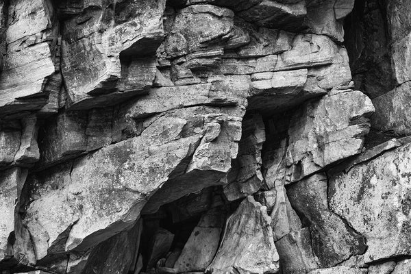 Black and white landscape photograph of dramatic, jagged layers of rock in the wall of a river canyon.
